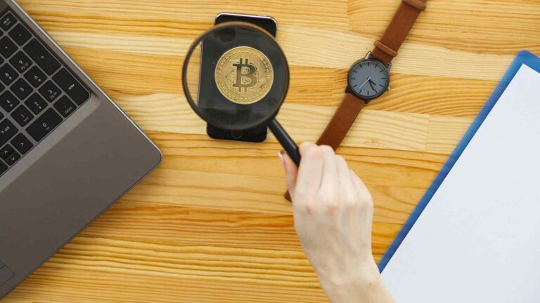 Lupa sobre bitcoin em mesa Banco Central publica regra que limita propagandas e ofertas de criptomoedas aos clientes